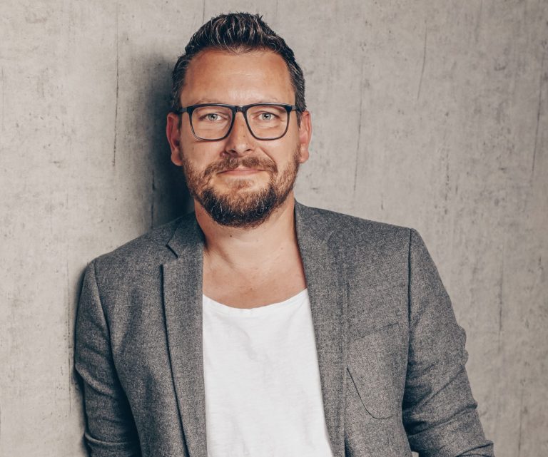 Mann mit Brille und Bart, trägt ein graues Sakko vor neutralem Hintergrund. Christian Riess 